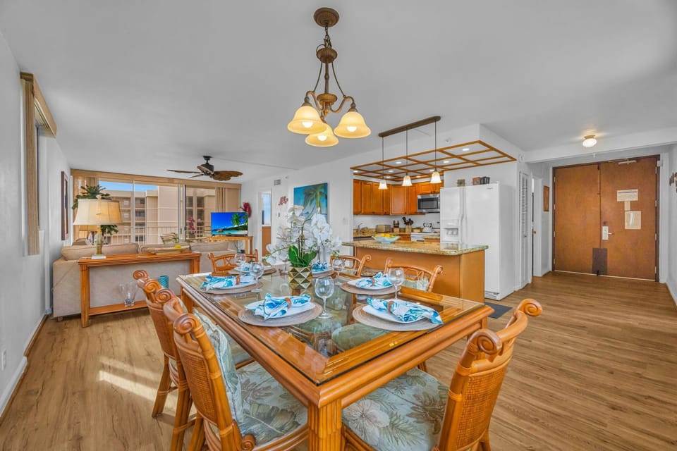 Glass‑top dining table with ornate chairs and chandelier, framed by the open layout connecting kitchen and living room.