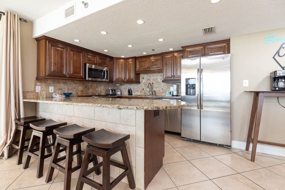 The modern kitchen features rich wooden cabinetry, a spacious granite breakfast bar with seating, and a sleek breakfast bar