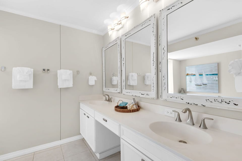 Pamper yourself in this pristine bathroom featuring dual vanities, weathered wood mirrors, and coastal touches that create your perfect morning routine.