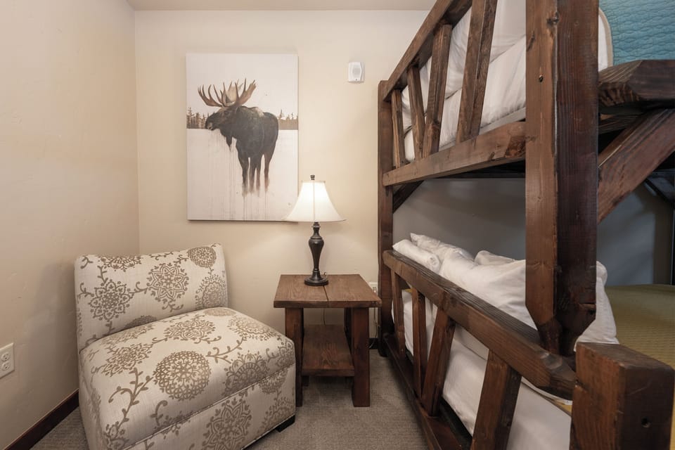 - Family friendly bunk room with sturdy wood beds, reading light, and cozy chair - Moose artwork and soft textiles create a warm mountain lodge theme - Great space for kids or friends with a mix of charm, comfort, and function
