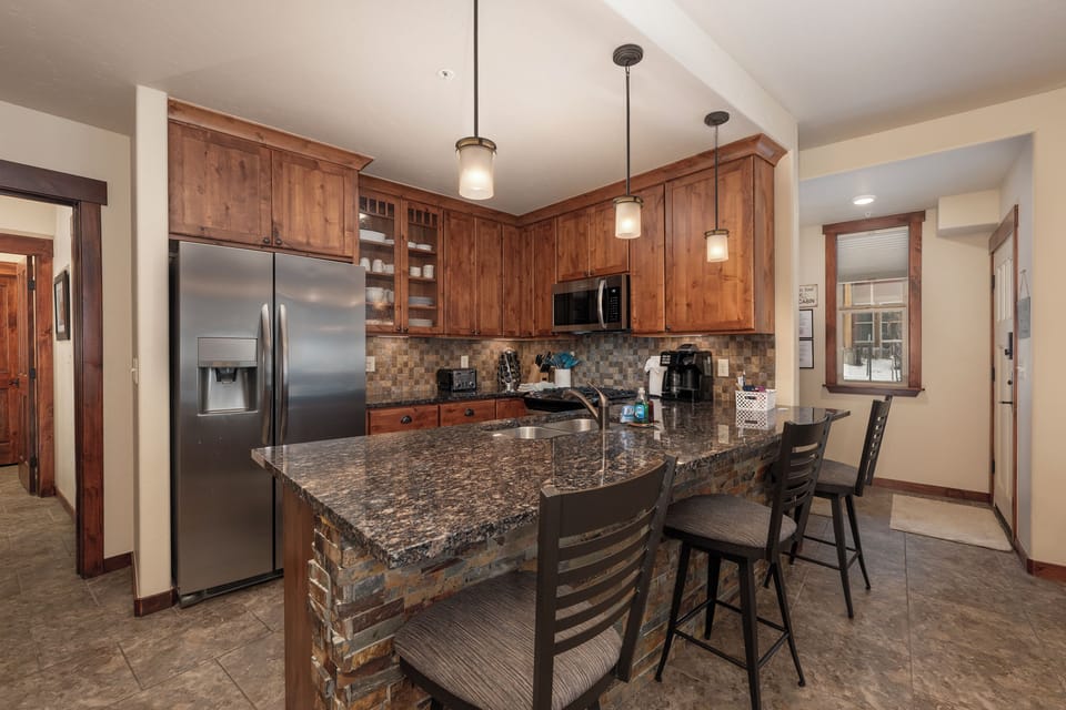 - Fully stocked kitchen with granite island, bar seating, and pendant lighting - Stainless steel fridge and microwave pair beautifully with custom cabinetry - Ideal for morning coffee, group meals, or casual snacks at the counter