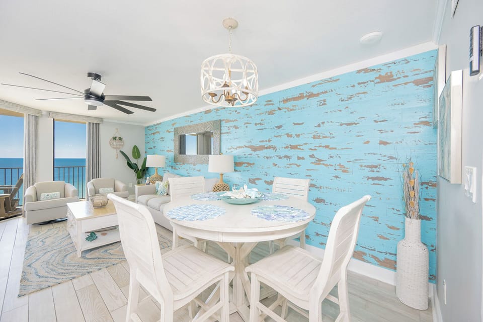Brightly decorated living space features a round dining table, comfortable seating, and expansive views of the beach