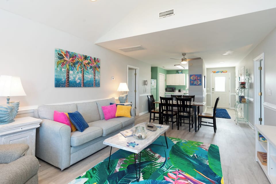 Your bright, tropical-themed living space features comfortable seating and vibrant artwork, creating the perfect coastal retreat atmosphere.