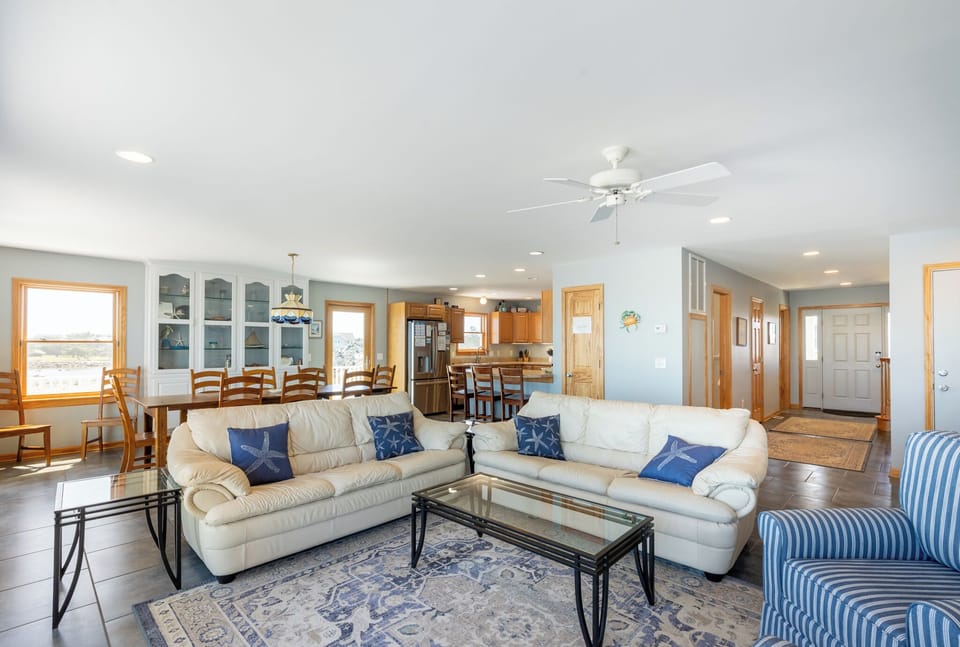 Spacious living area flows into dining and kitchen, offering you room to gather and relax. Plush white sofas, coastal blue accents, and natural light create a welcoming retreat.
