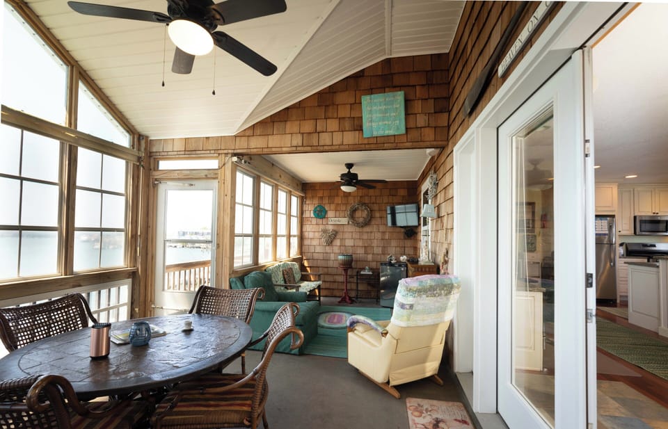 Settle into this breezy sunroom where coastal charm meets comfort. Natural light pours through wraparound windows as ceiling fans keep you cool. Your perfect spot for morning coffee or evening relaxation with water views just beyond the door.