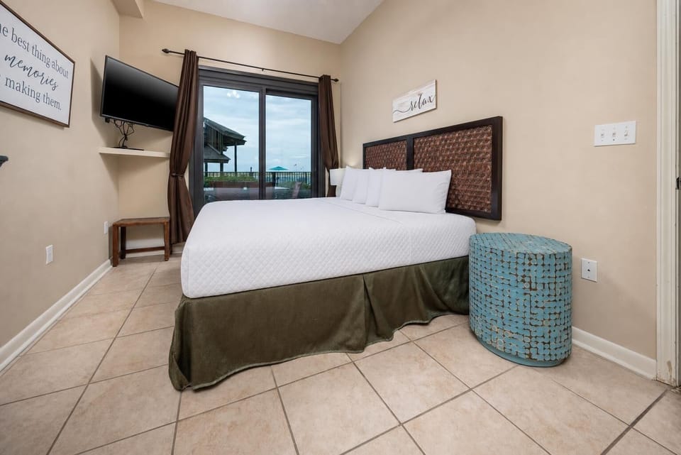 Brightly decorated master bedroom features a king bed, a mounted TV, leading to the outdoor beach patio