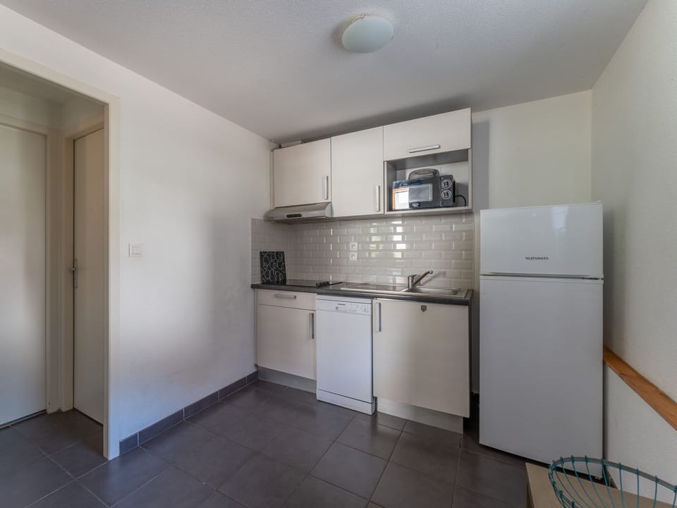 The well-equipped kitchenette with full-size refrigerator, ceramic hob, microwave and dishwasher — everything in place for relaxed self-catering between days on the lake and the Atlantic coast.