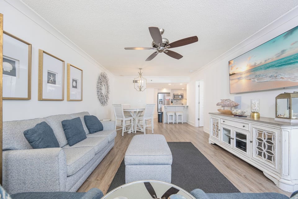Living area features a light gray sofa queen sleeper, a dining table, and a view of the kitchen with bar seating
