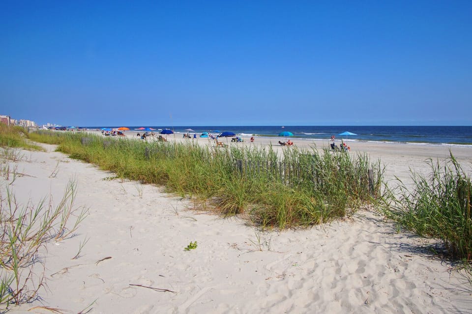 Dune grass and beach umbrellas steps from Crescent Sands K5, a 2-bedroom Crescent Beach vacation rental