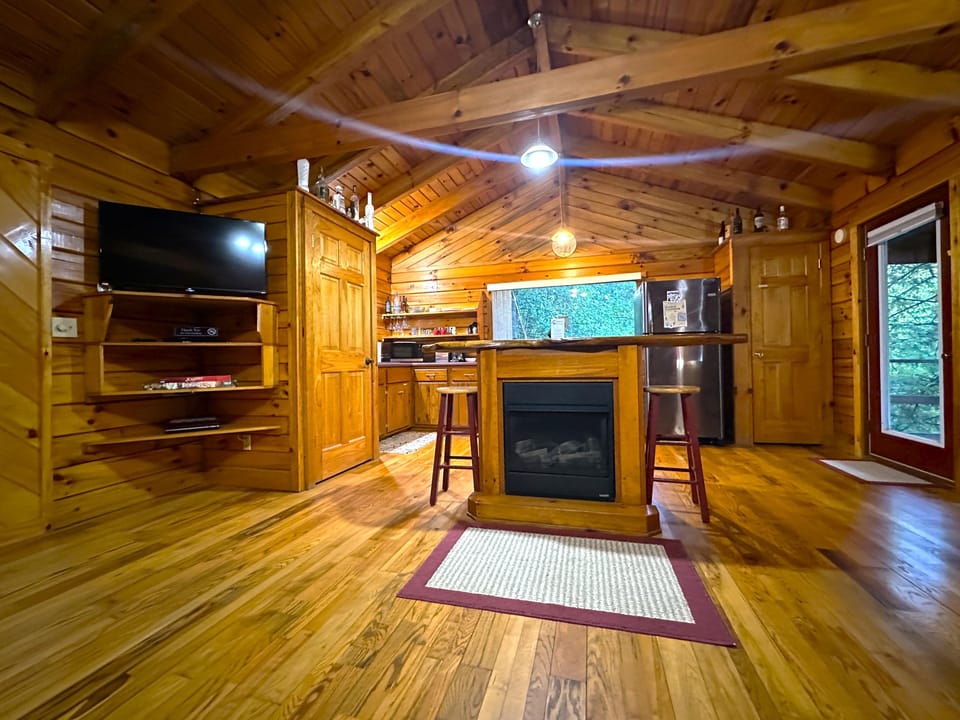 Central island with built-in fireplace and two wooden stools anchors the knotty pine kitchen and living area.