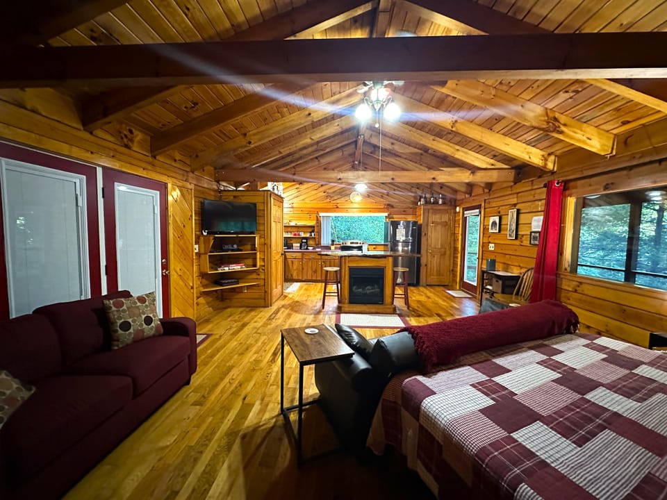 Open-concept living area with vaulted pine ceiling, wood floors, red sofa, and kitchen island with stools.