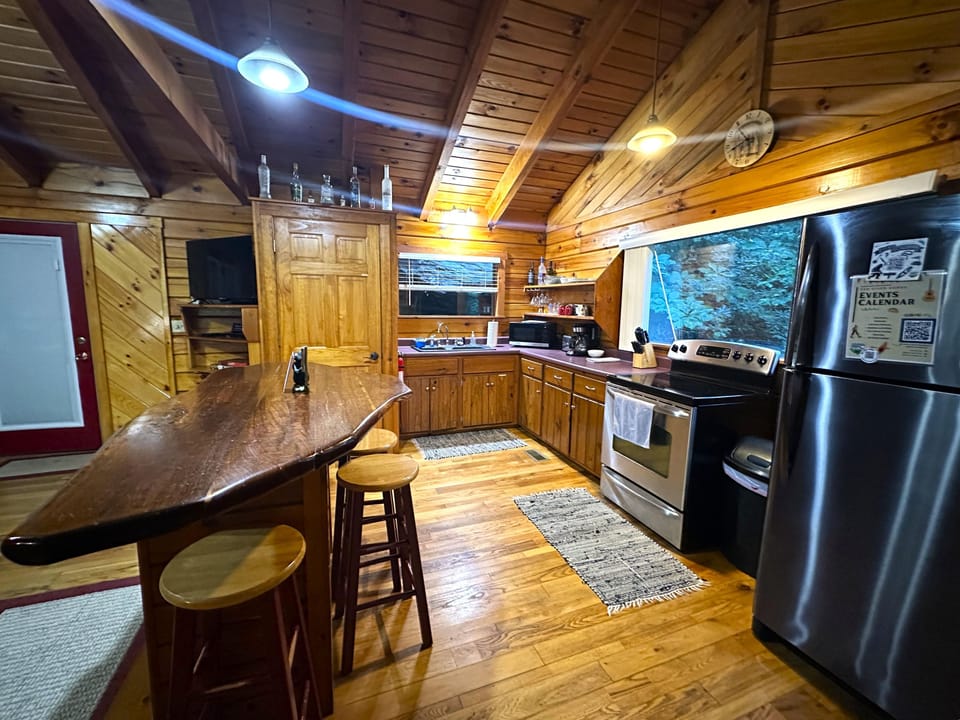 Kitchen with natural wood cabinetry, stainless steel appliances, a surfboard-shaped breakfast bar, and angled wood-paneled ceiling.