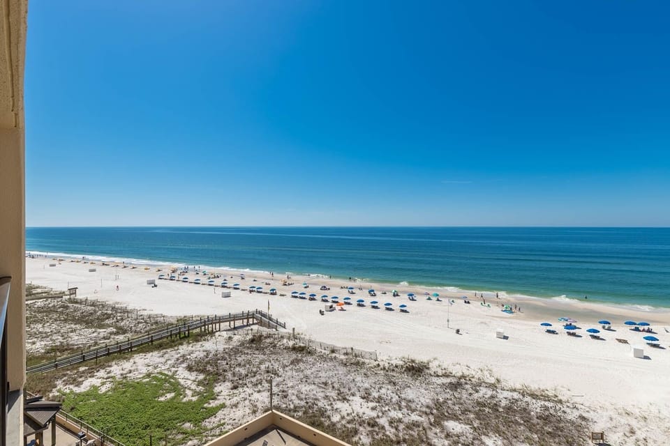 Stunning view of the serene beach and vibrant umbrellas under a clear blue sky from a spacious balcony