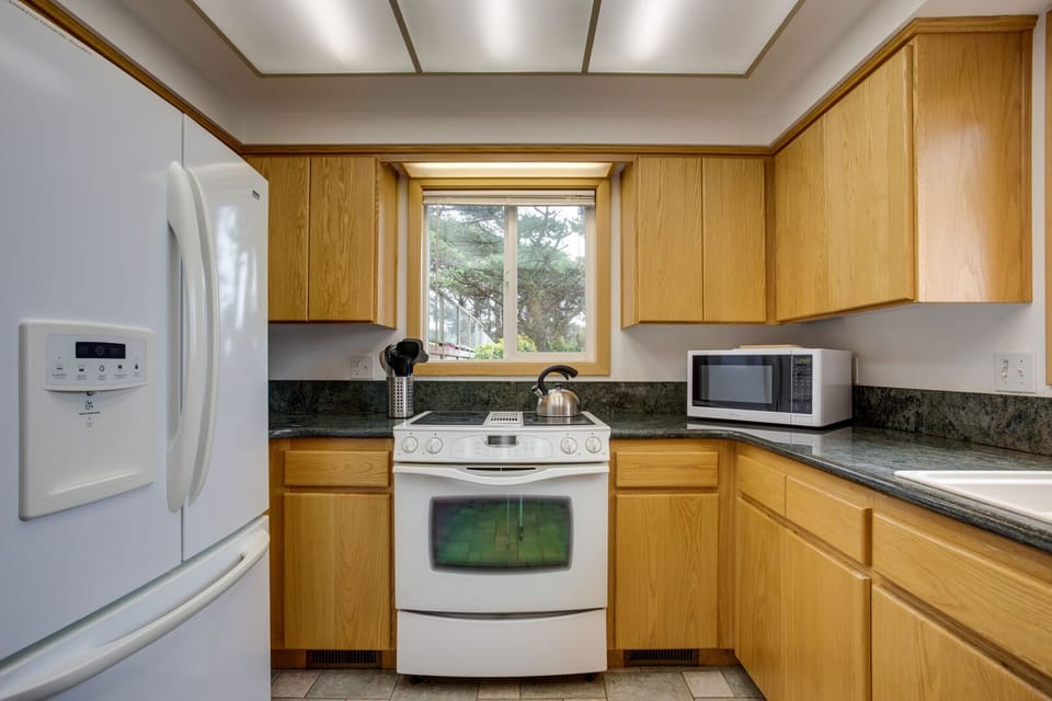 The bright kitchen is surrounded by trees.