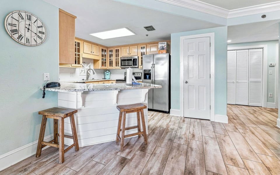 Kitchen area featuring light wood cabinetry, granite countertops, stainless appliances, and breakfast bar with wooden stools