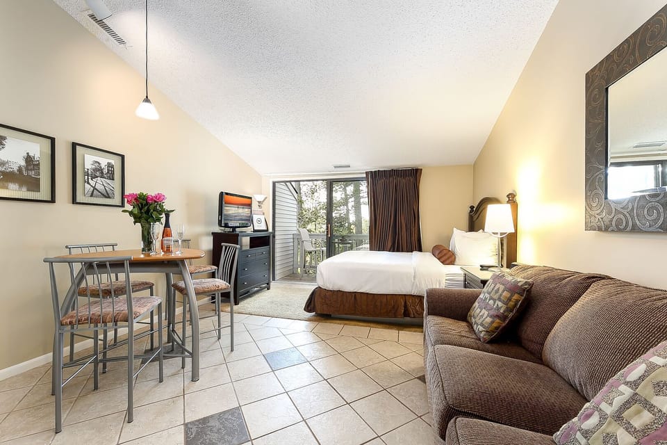 The unit is a studio layout featuring a queen-size bed, a queen-size sleeper sofa, a dining table for four, a TV, a balcony with a lake view, and offers a comfortable stay.