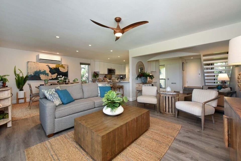Bright and airy living room with plush seating, ceiling fan, and large windows framing lush garden views.