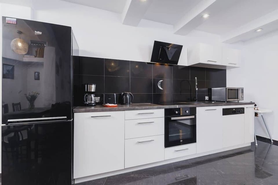 A modern kitchen equipped with glossy dark cabinets, a white countertop, and state-of-the-art appliances. The reflective surfaces amplify the light, making the space feel more expansive.