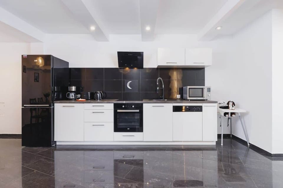 A modern kitchen equipped with glossy dark cabinets, a white countertop, and state-of-the-art appliances. The reflective surfaces amplify the light, making the space feel more expansive.