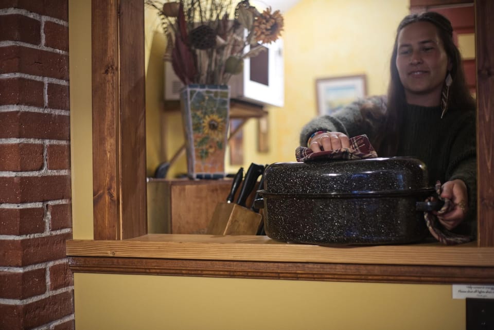 Kitchen pass-through with yellow walls, wooden trim, brick column, and a speckled roasting pan being handled.