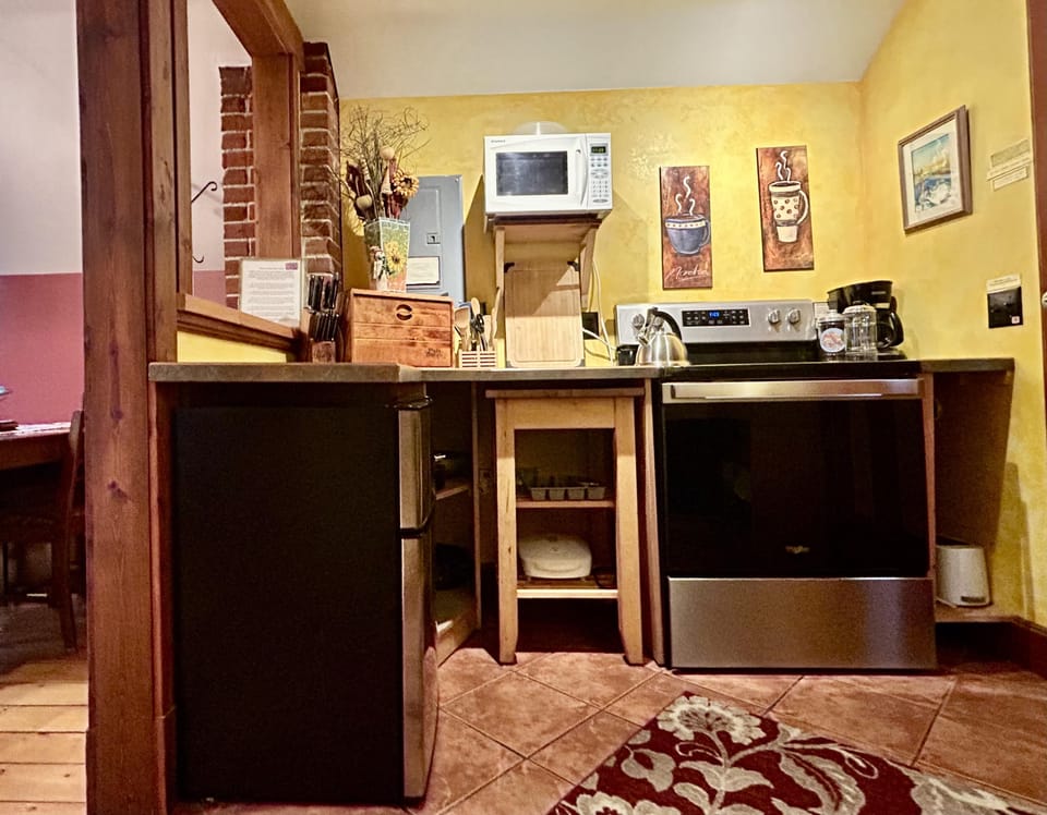 Kitchen corner with stainless steel stove, black mini fridge, wooden shelves, and yellow textured walls.