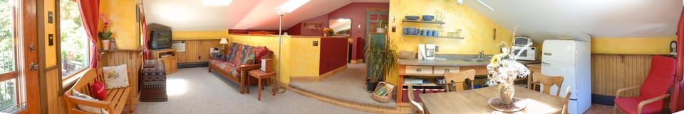 Bedroom features sloped yellow walls, wood paneling, a patterned futon sofa, red curtains, and a mounted air conditioner.