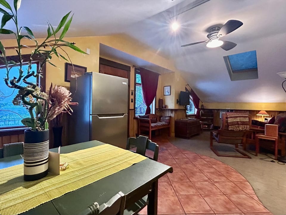 Bedroom area with sloped ceiling, skylight, mounted TV, and wood-framed seating under burgundy curtains.