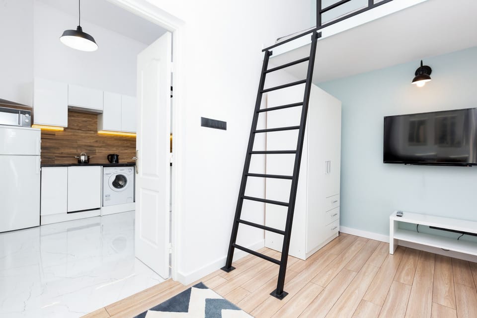 A compact setup with a loft ladder, wall-mounted TV, and sleek decor for practical living.