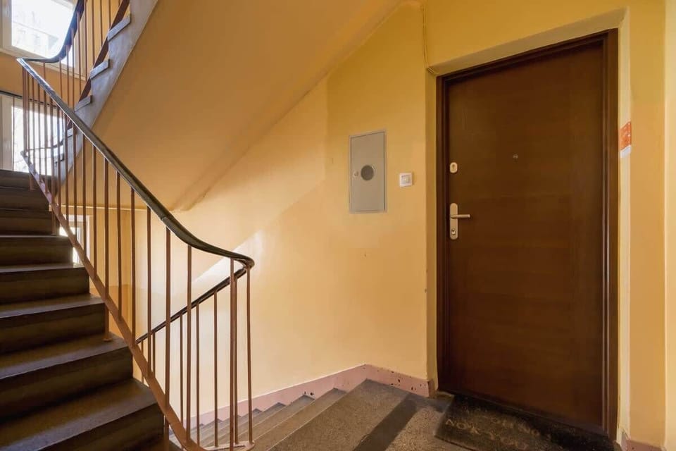 A stairwell in a residential building, with yellow-painted walls, metal railings, and a wooden door at the top landing.