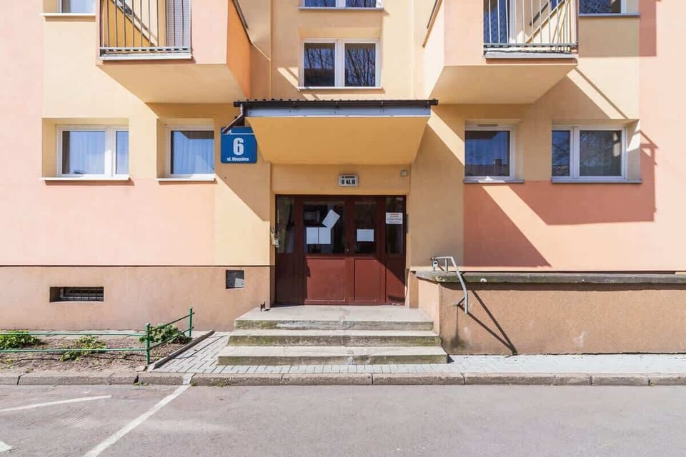 The exterior of an apartment building painted in a pale yellow, with a parking area and a few visible windows.