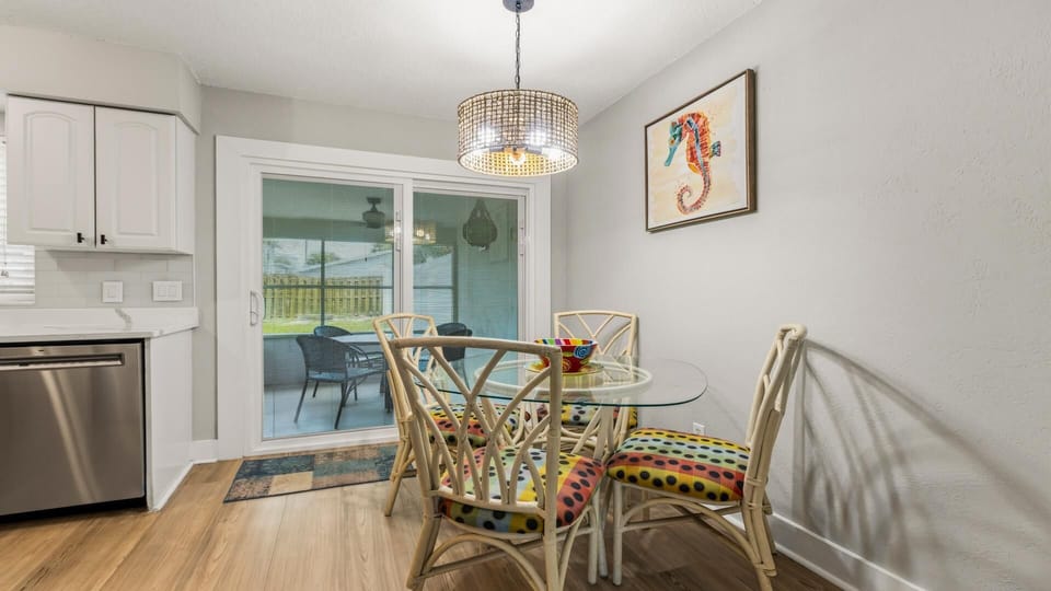 Dining area with glass-top table, rattan chairs featuring colorful polka dot cushions, and sliding doors to patio.