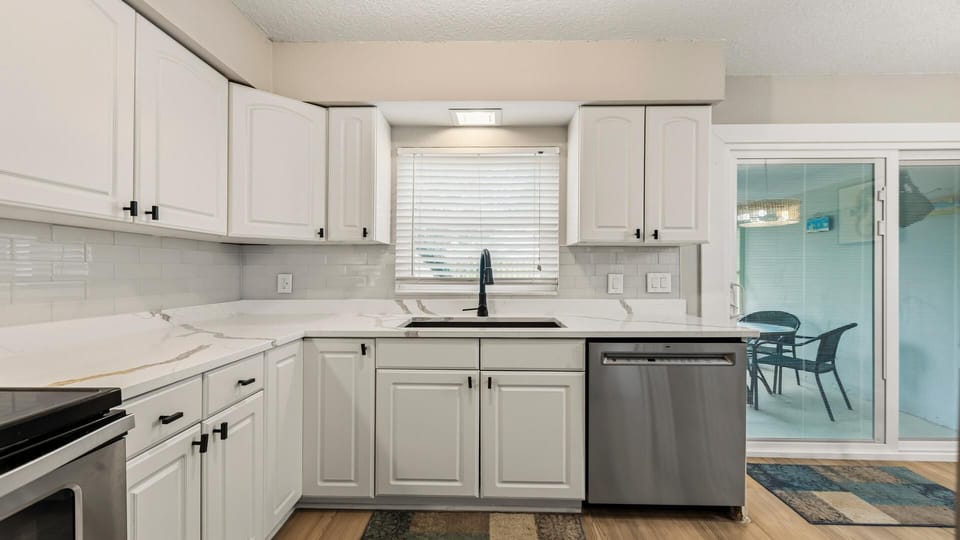 White cabinetry and marble-effect countertops surround a black faucet and stainless dishwasher near sliding glass doors.