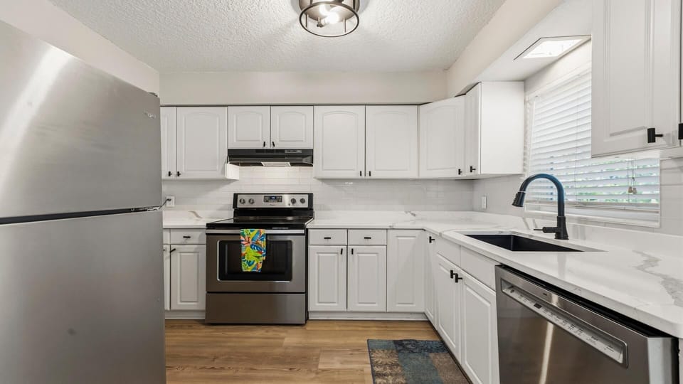 White cabinetry lines the kitchen with marble-patterned countertops, black hardware, and stainless steel appliances.