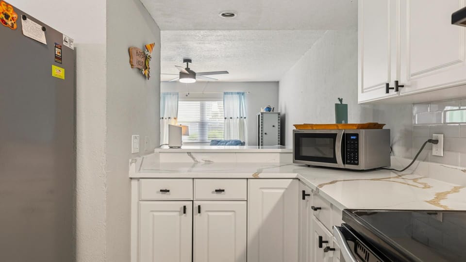 White cabinetry lines the kitchen with marble-look countertops and a stainless steel microwave on the corner.