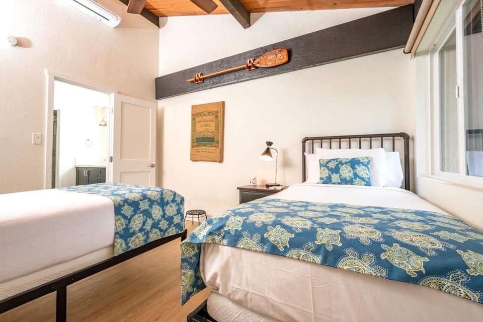 Stylish guest room with twin beds, vaulted ceilings, tropical prints, and bright views of lush garden greenery    
