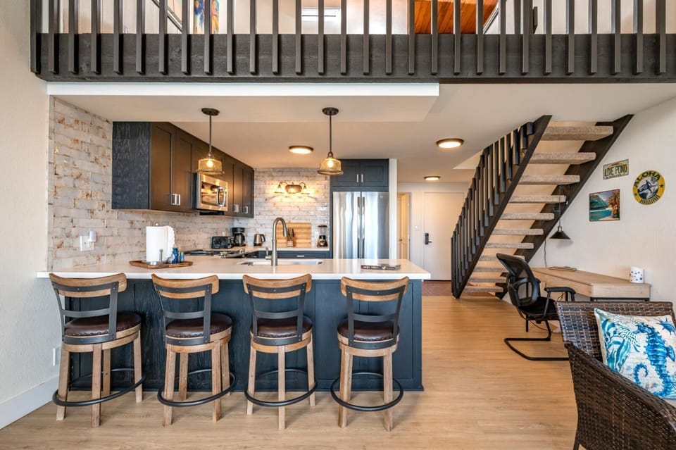 This modern kitchen features sleek dark cabinetry, pendant lighting, and a brick backsplash that adds rustic charm    