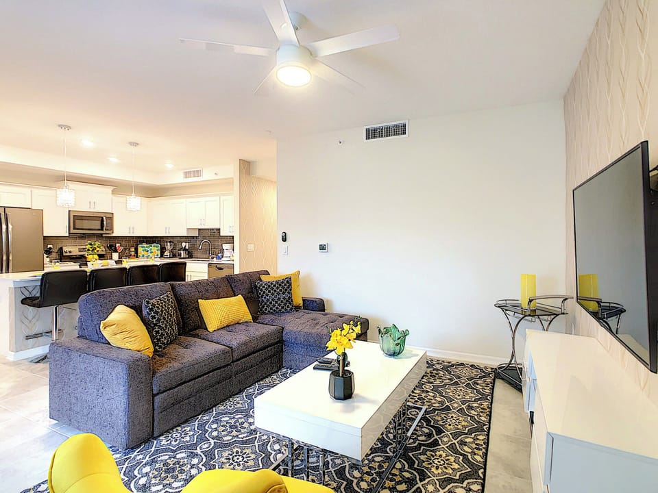 Open living area with sectional sofa, flat-screen TV, and kitchen