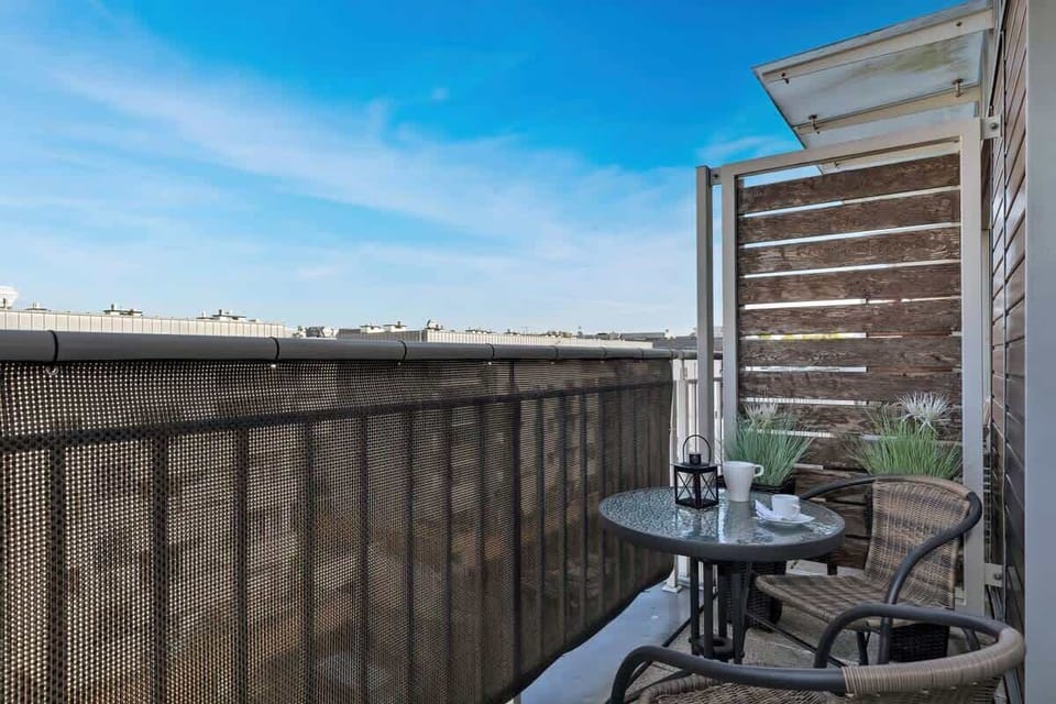 A view from a balcony showing a cityscape or residential area, with outdoor seating and a table with a cup on it.