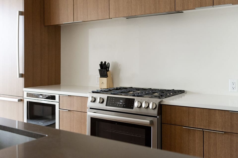 Chef's gas range in the kitchen with white quartz countertops and backsplash, wooden cabinets with chrome hardware