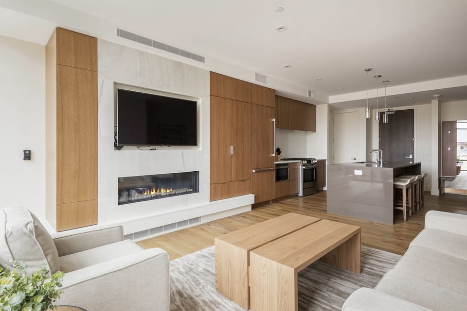 Open floor plan with living room, kitchen, and dining area, wooden and quartz accents, hardwood floors throughout, large flat screen TV mounted above the fireplace