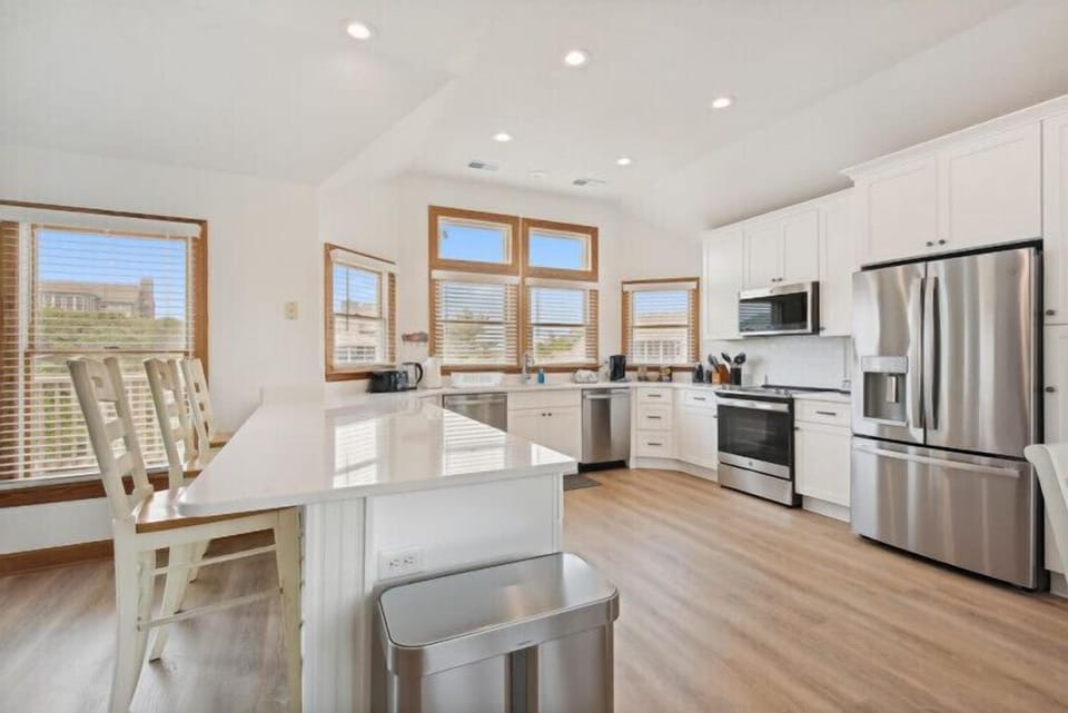 Step into your bright, open kitchen where white cabinetry meets stainless steel appliances and abundant natural light pours through wood-trimmed windows—perfect for preparing family meals or morning coffee.