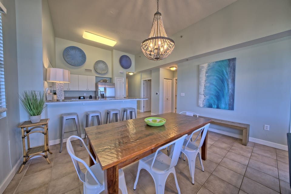 Dining table for six, four barstools at the kitchen bar, a full kitchen, and a beaded chandelier tying it all together. Everyone eats together here. No splitting the group, no cramped counters — just one big space built for the whole crew.