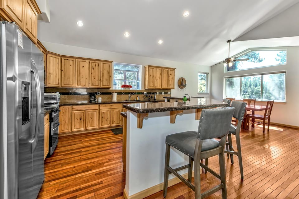 Natural wood cabinets and granite countertops surround the kitchen, with a breakfast bar and gray leather stools.