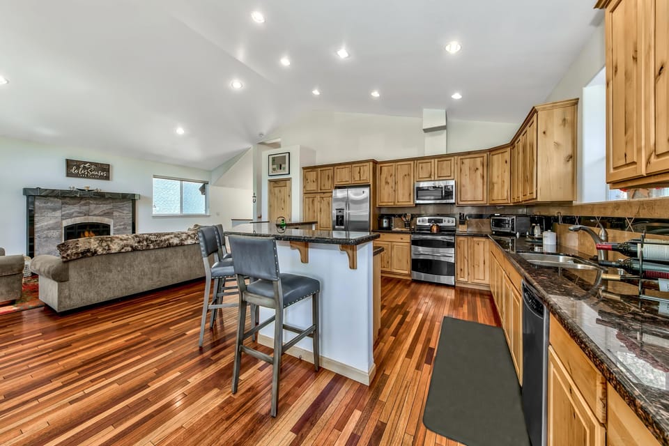 Open kitchen with natural wood cabinets, granite countertops, and three leather bar stools at the island.