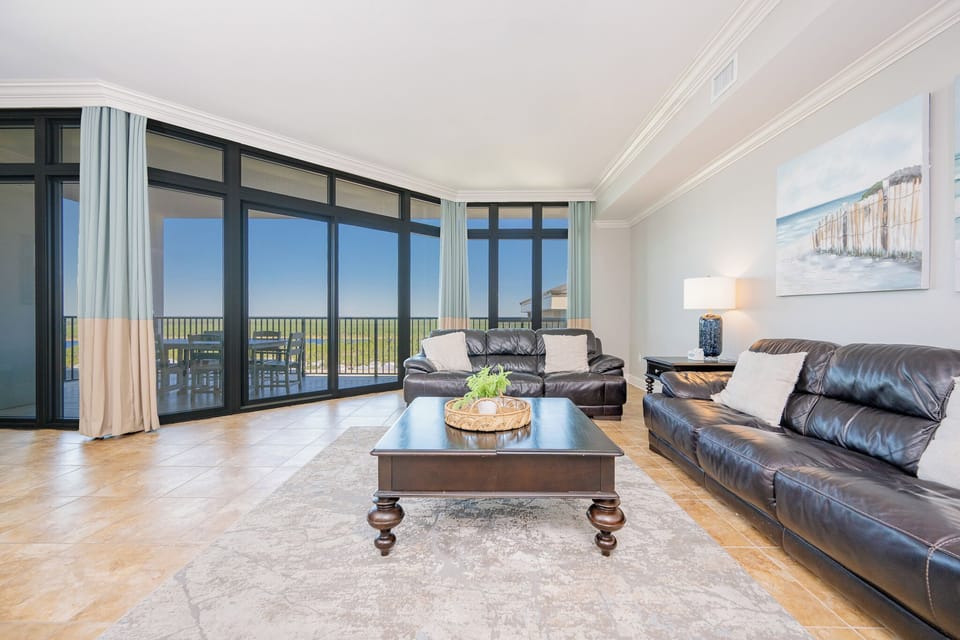 Bright living area with plush leather sofas, a stylish coffee table, and expansive windows offering a beautiful outdoor view