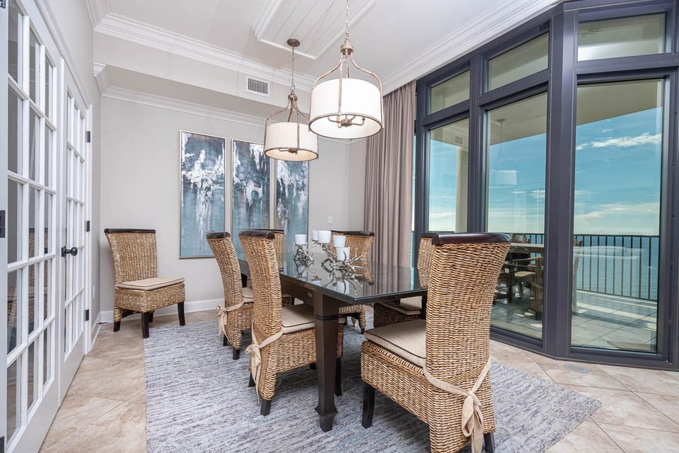 This dining area features stylish woven chairs around a glass table, with stunning beachfront views through large windows