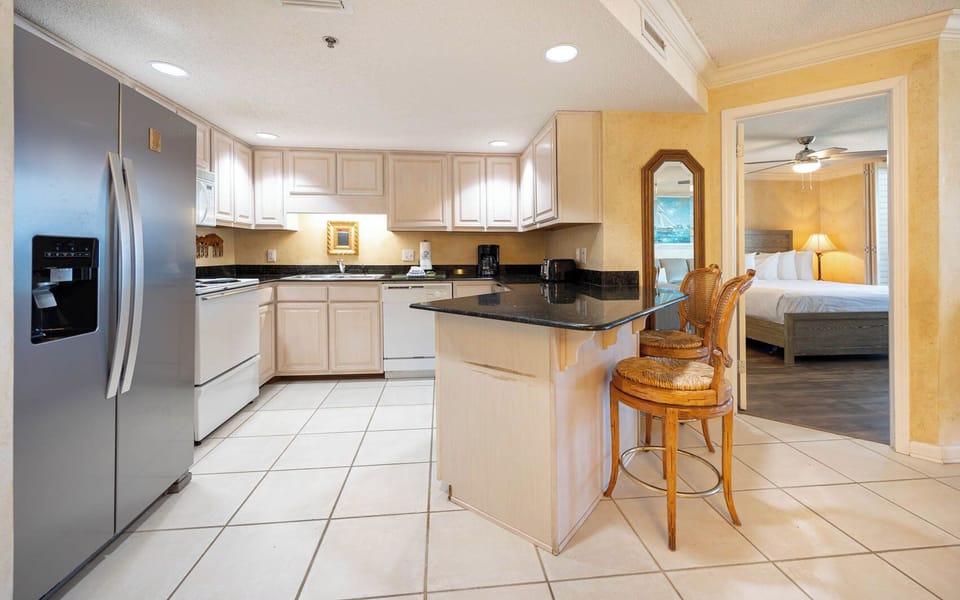 Kitchen features a breakfast bar with seating, granite countertops, large refrigerator, and coffee maker