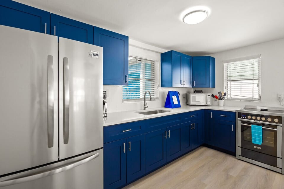 Siesta Key beach retreat kitchen with ocean-blue cabinets, modern stainless appliances, and a sunny sink view—styled for relaxed prep and laid-back coastal living.