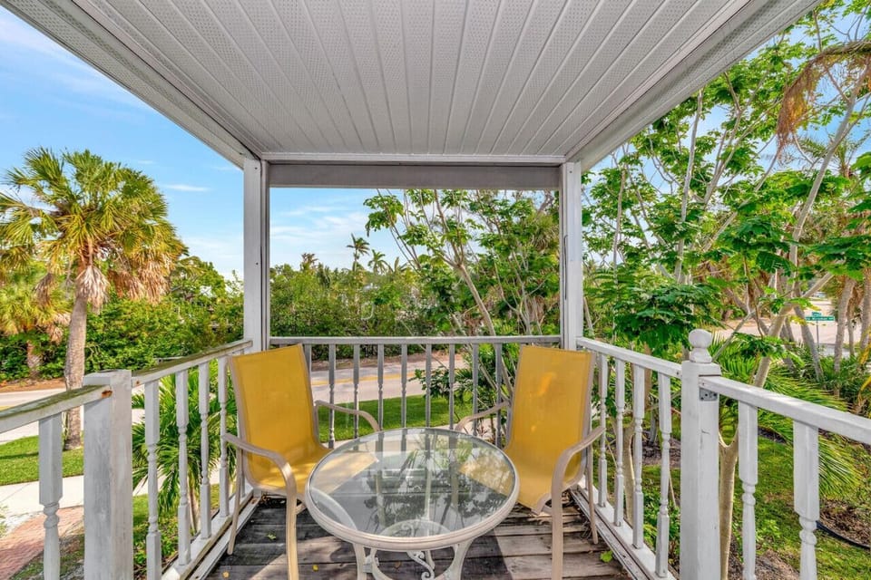 Siesta Key Beach private porch featuring yellow chairs, a glass-top table, and palm-filled views perfect for peaceful coastal lounging.