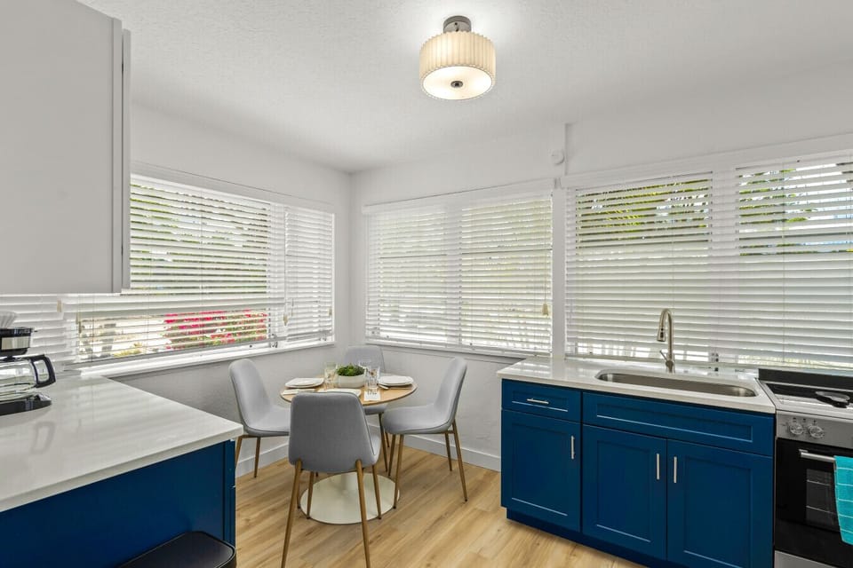 Modern kitchen and dining space in Siesta Key featuring vibrant blue cabinetry, white countertops, and a cozy dining nook bathed in natural light from sun-filled windows.